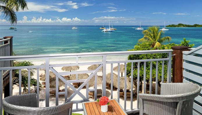 Thatched-roof overwater villas stand on stilts above clear turquoise water at all-inclusive resorts, with lounge chairs and steps leading directly into the sea, under a bright blue sky.